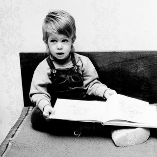 Young child reading book intently indoors.