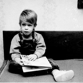 Young child reading book on bed.
