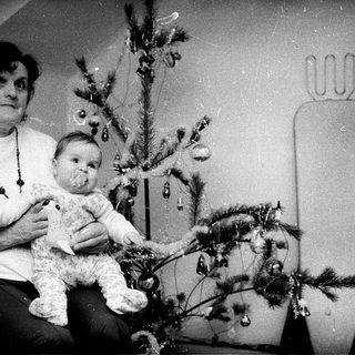 Woman holding baby beside decorated Christmas tree.