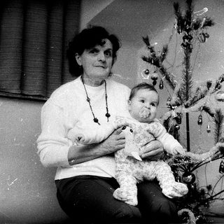 Woman holding baby beside decorated Christmas tree.