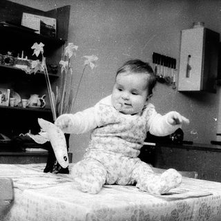 Baby sitting on table holding paper airplane.