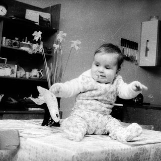 Baby sitting on table holding paper airplane.