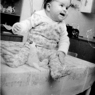 Baby wearing fluffy sweater sitting on table.