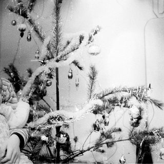 A child holds a baby beside a decorated Christmas tree.