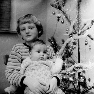 A child holds a baby beside a decorated Christmas tree.