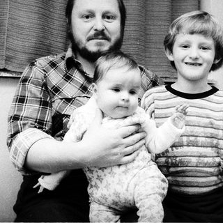 Family portrait with man, baby, and young boy near Christmas tree.