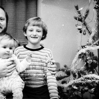 Family portrait with man, baby, and young boy near Christmas tree.
