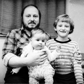 Family portrait with man, baby, and young boy near Christmas tree.
