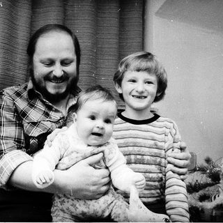 Family portrait with man holding baby, boy standing beside them near Christmas tree.
