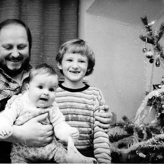 Family portrait with man holding baby, boy standing beside them near Christmas tree.