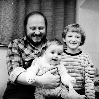 Family portrait with man holding baby, boy standing beside them near Christmas tree.