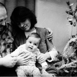 Family portrait with parents holding a baby near a Christmas tree.