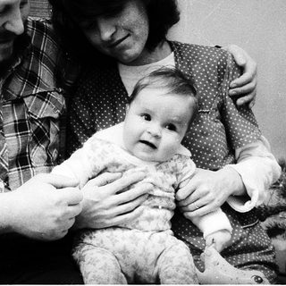 Family portrait with parents holding a baby near a Christmas tree.