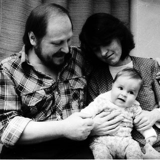 Family portrait with parents holding a baby near a Christmas tree.