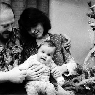 Family portrait with parents holding a baby near a Christmas tree.