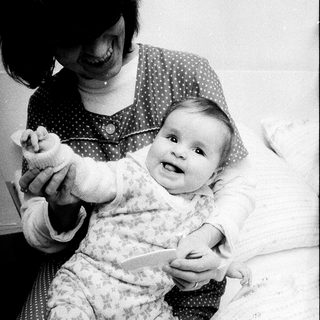 A woman plays with a smiling baby indoors.
