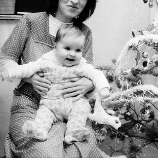 A woman holding a baby near a decorated Christmas tree.