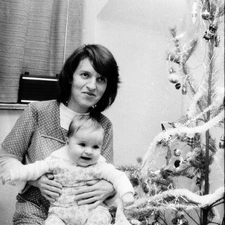 A woman holding a baby near a decorated Christmas tree.