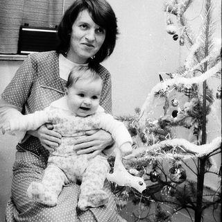 A woman holding a baby near a decorated Christmas tree.