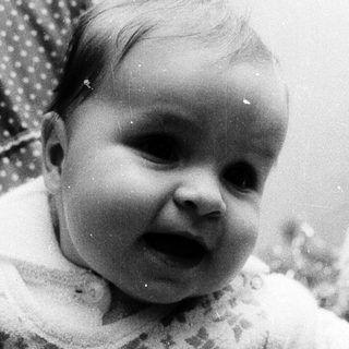 Baby in vintage outfit, smiling indoors.