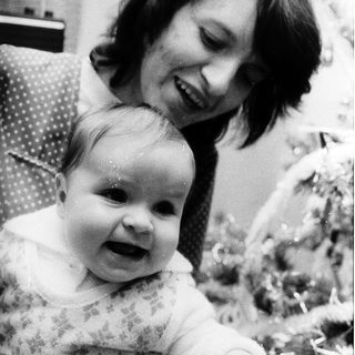 A woman smiling while holding a cheerful baby indoors.