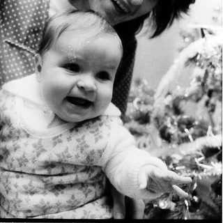 A woman smiling while holding a cheerful baby indoors.