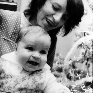 A woman smiling while holding a cheerful baby indoors.