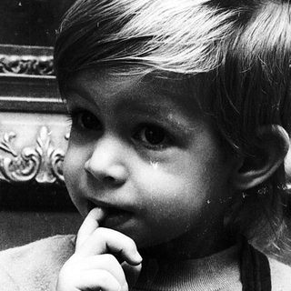 Young child biting finger in indoor setting.