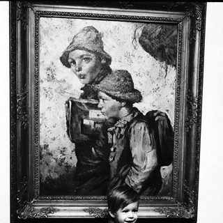 Child posing beside vintage portrait of woman in outdoor attire.