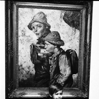 Child posing beside vintage portrait of woman in outdoor attire.