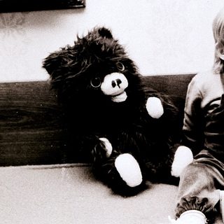 Young child sitting with black teddy bear.