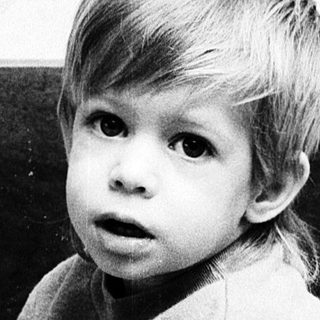 Young child sitting on floor, looking surprised.