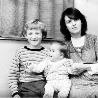 Family portrait with mother, older child, and baby near Christmas tree.