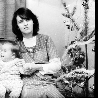 Family portrait with mother, older child, and baby near Christmas tree.