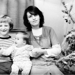 Family portrait with mother, older child, and baby near Christmas tree.