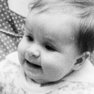 A woman holding a smiling baby indoors near holiday decorations.