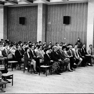 Formal meeting or conference with speaker addressing seated audience.