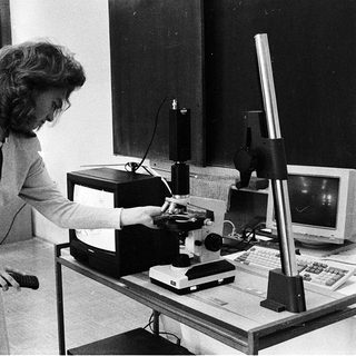 Scientist operating vintage microscope with computer equipment.