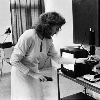 Scientist operating vintage microscope with computer equipment.