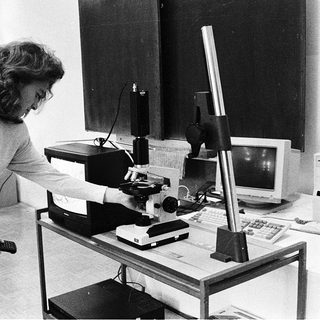 Woman operating vintage microscope with camera attachment.