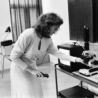 Woman operating vintage microscope with camera attachment.