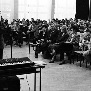 Man speaking to audience at indoor lecture or meeting.