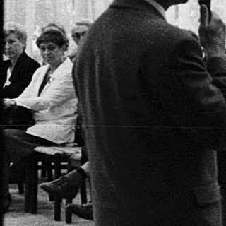 Man speaking to audience at indoor lecture or meeting.