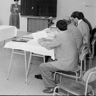 Classroom seminar or meeting with participants seated and a speaker presenting.