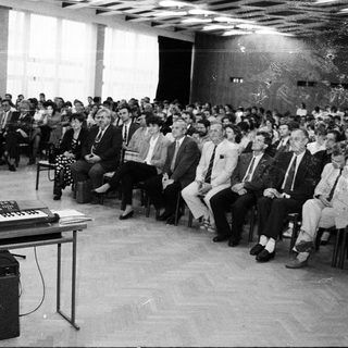 Large indoor audience listening to a lecture or performance.