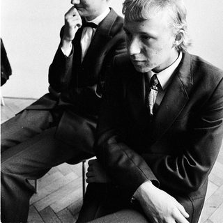 Two men in suits sitting thoughtfully indoors.