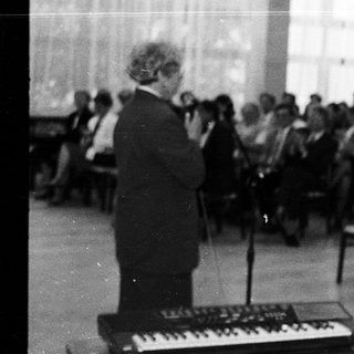 Man speaking at a lecture or event with keyboard instrument.