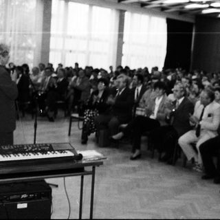 Man speaking at a lecture or event with keyboard instrument.