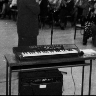 Man speaking at a lecture or event with keyboard instrument.