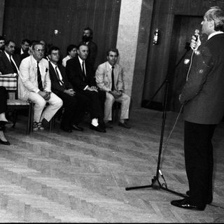 Formal indoor gathering with speaker addressing seated audience.